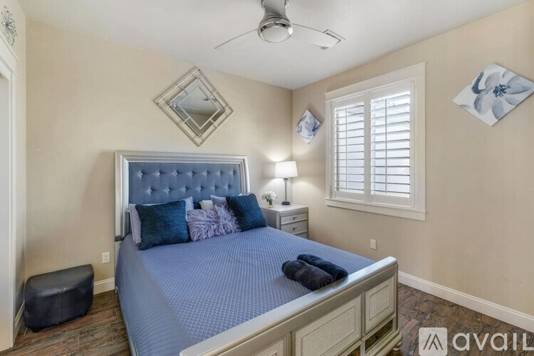 A bedroom with a blue bedspread and a ceiling fan.