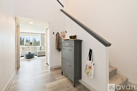 A hallway with a staircase and a cabinet with a coat hanging on it.