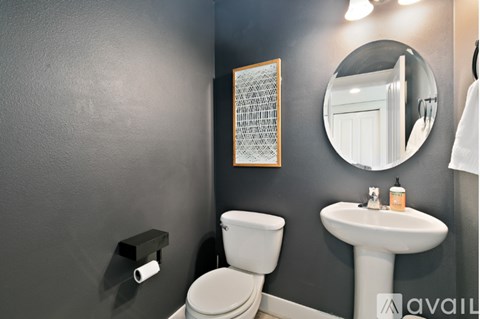 A bathroom with a toilet, sink, mirror, and a picture on the wall.