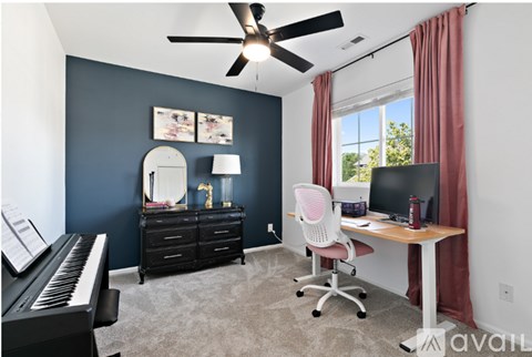 A room with a piano, a desk with a computer, and a ceiling fan.