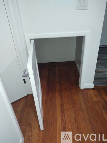 A white cabinet with a door open in a room with wood flooring.