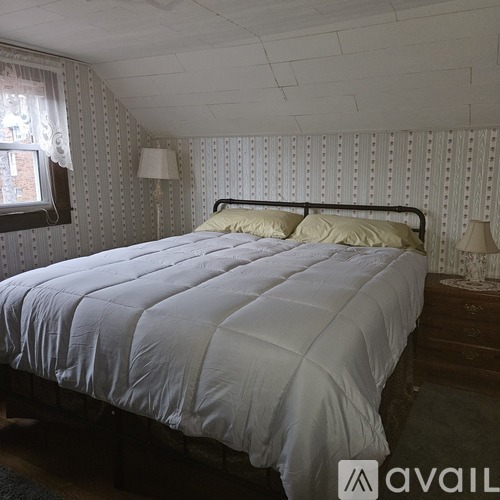 A bed with a white comforter and two yellow pillows in a room with white walls.