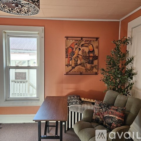 A living room with a sofa, a table, a window, a plant and a picture on the wall.