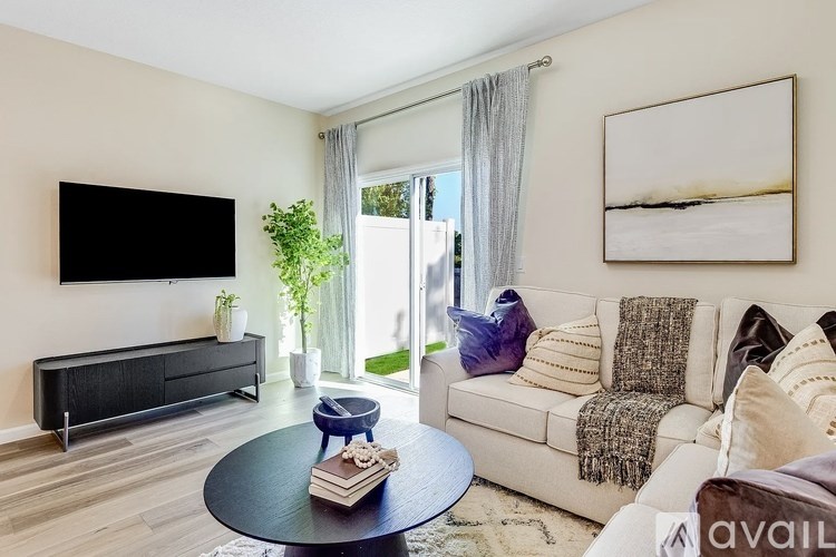 A living room with a black sofa, a coffee table, and a flat screen TV mounted on the wall.