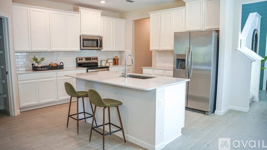 A kitchen with white cabinets and a white island with two chairs.