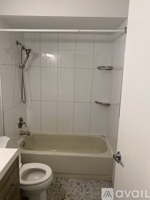 A white tiled bathroom with a toilet, tub, and shower.