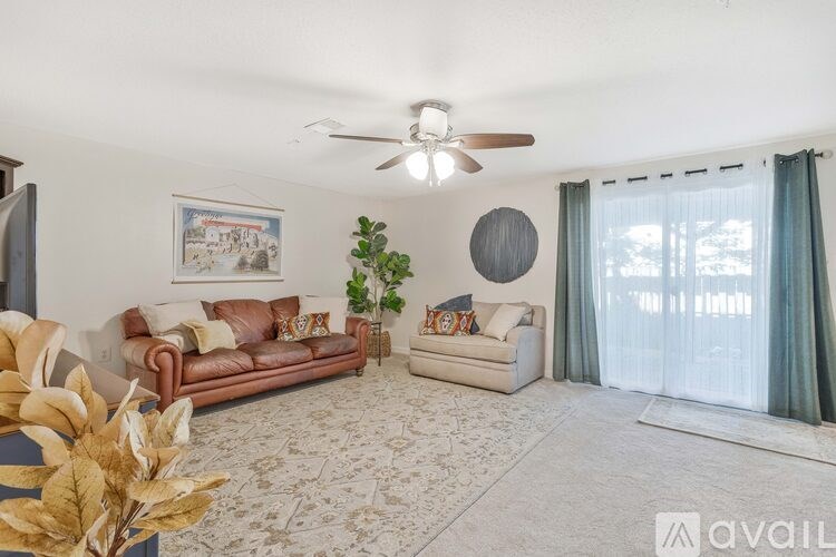 A living room with a brown leather couch, a white couch, a rug, and a ceiling fan.