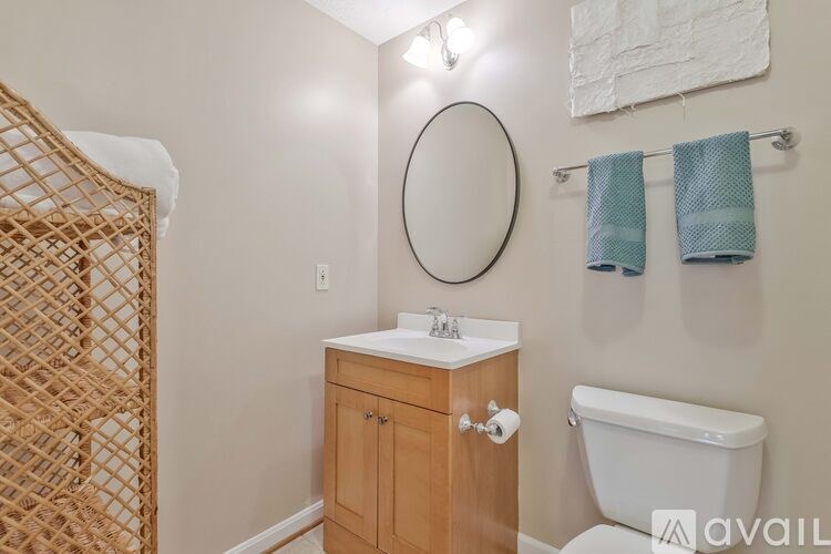A bathroom with a white toilet, a wooden cabinet, a round mirror, and a towel rack with two towels.
