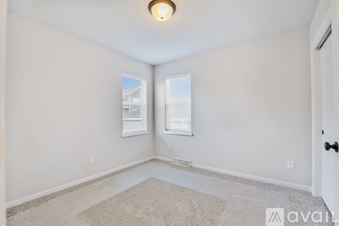 A room with a carpeted floor, two windows with blinds, and a door.