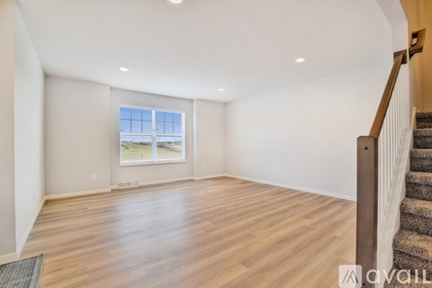 A spacious room with wooden flooring and a staircase on the right side.