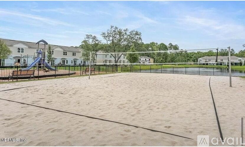 A sandy playground area with a slide and fencing in front of apartment buildings.