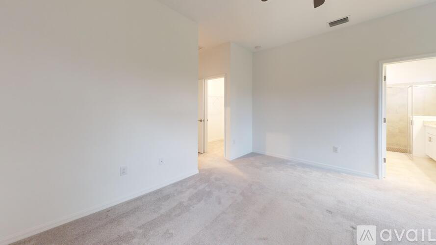 A spacious room with carpeted floor and white walls, with a door on the right side.