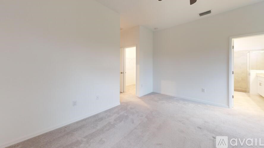 A spacious room with carpeted floor and white walls, with a door on the right side.