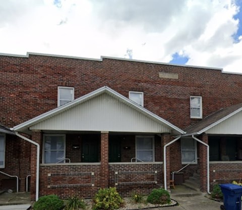 A red brick house with a white roof and a blue trash bin in front.