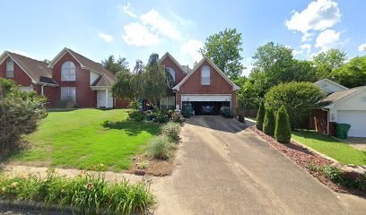 A residential street with houses on both sides and a driveway in the foreground.