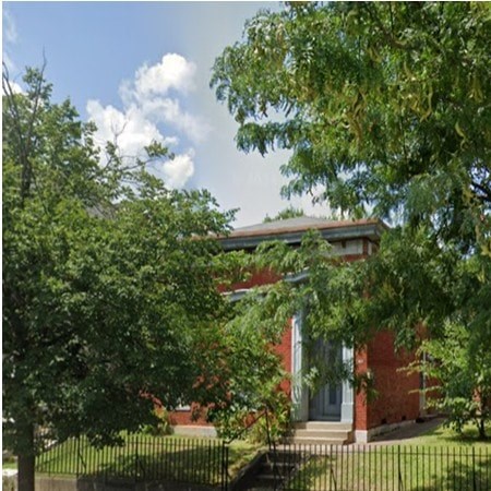 A red brick house with a white door and a tree in front.