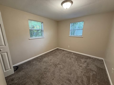 A room with carpeted floor and two windows.