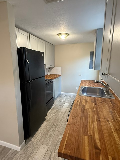 A black refrigerator is in a kitchen with a wooden counter top.