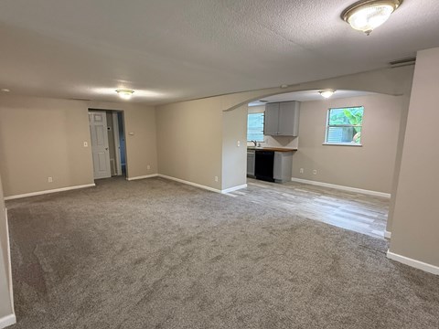 A spacious room with carpeted floor and a small kitchenette in the corner.