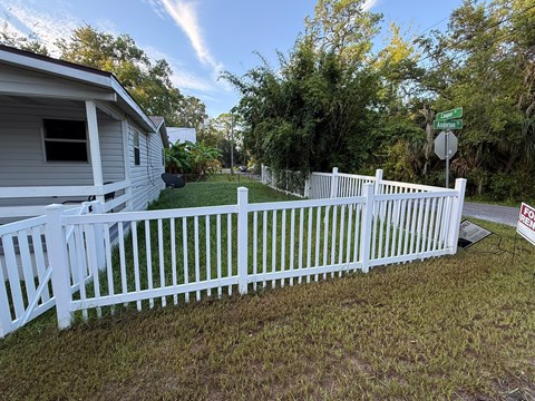 A white picket fence surrounds a house with a "For Sale" sign in the yard.