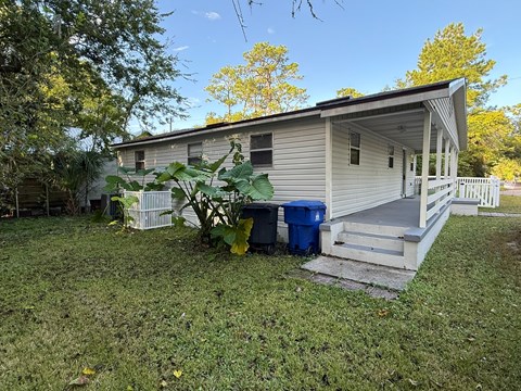 A house with a porch and a blue trash can in front.
