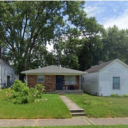 A house with a brick front and a porch is surrounded by greenery.