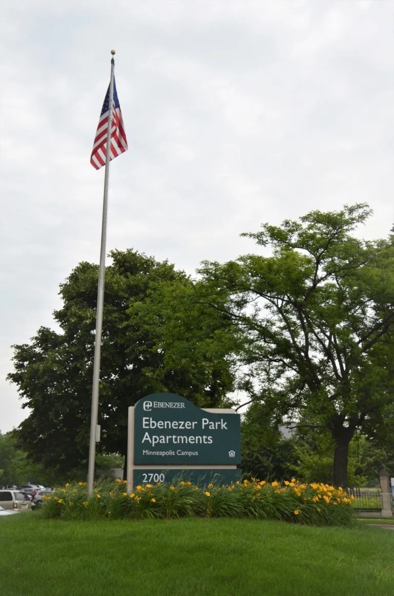 A sign for Ebenzer Park Apartments is in front of a flag pole.
