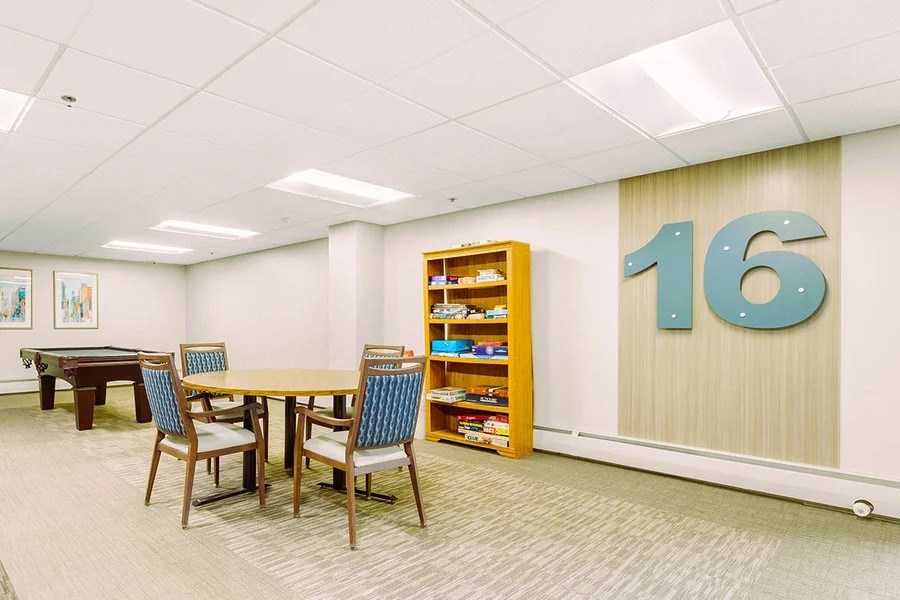 A conference room with a table, chairs, and a bookshelf with the number 16 on the wall.