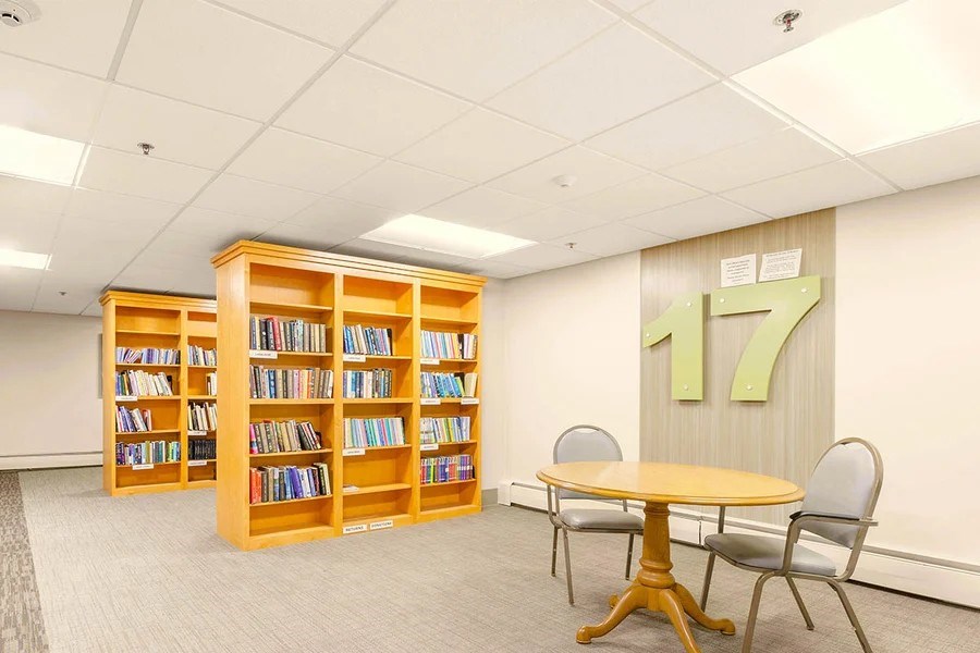 A room with a table, chairs and a bookshelf with the number 17 on the wall.