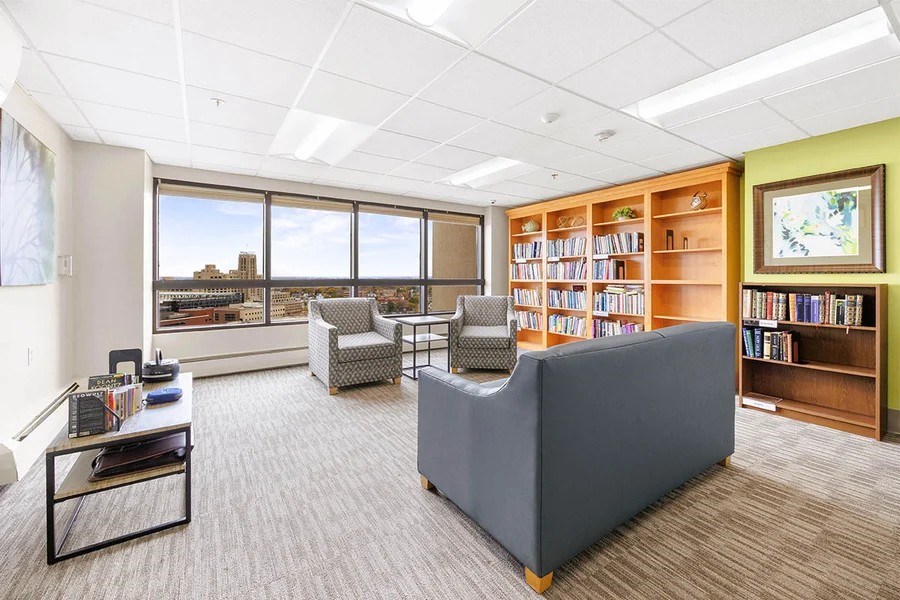 A room with a grey sofa, a coffee table, and a bookshelf filled with books.