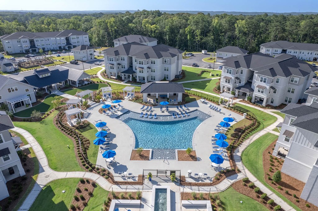 A large swimming pool surrounded by blue lounge chairs and umbrellas is the centerpiece of a resort-style community.
