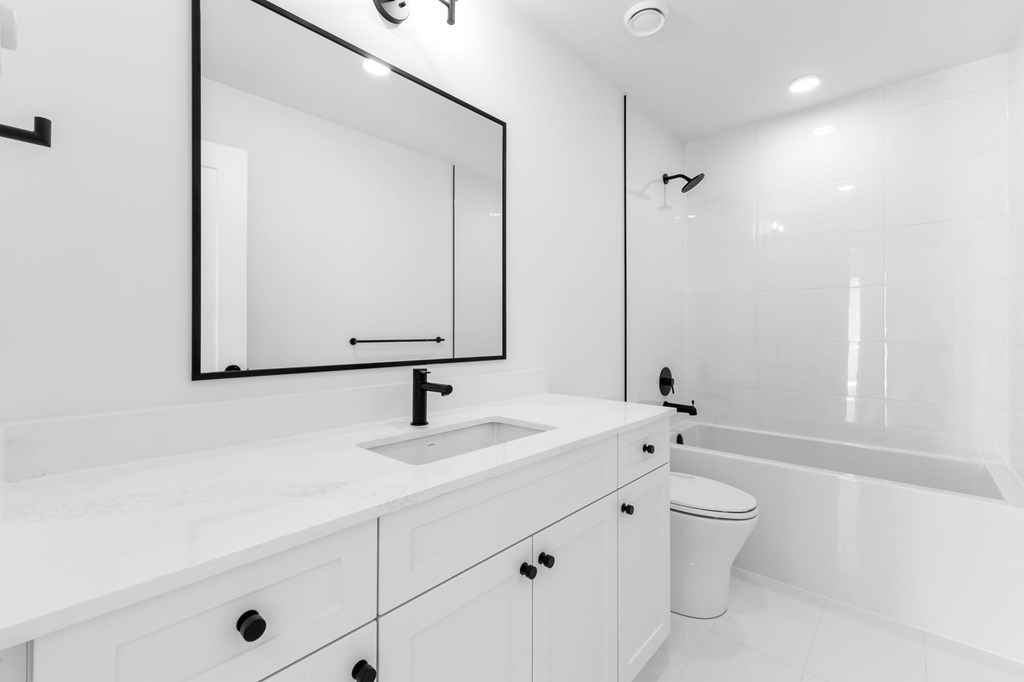 A white bathroom with a sink, mirror, and toilet.