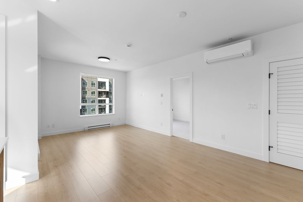 A spacious room with wooden flooring and a window with blinds.