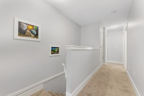 A hallway with two pictures on the wall and a carpeted floor.