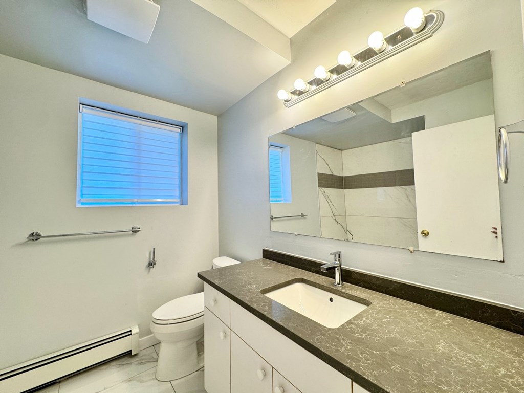 A bathroom with a toilet, sink, mirror, and window.
