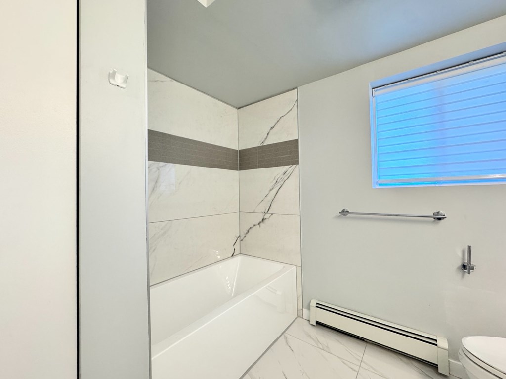 A white bathroom with a toilet, sink, and a window with blinds.