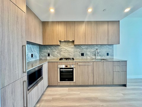 A modern kitchen with wooden cabinets and a stone backsplash.