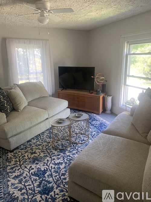 A living room with a sofa, a coffee table, a television, and a fan.