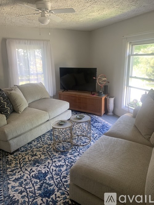 A living room with a sofa, a coffee table, a television, and a fan.