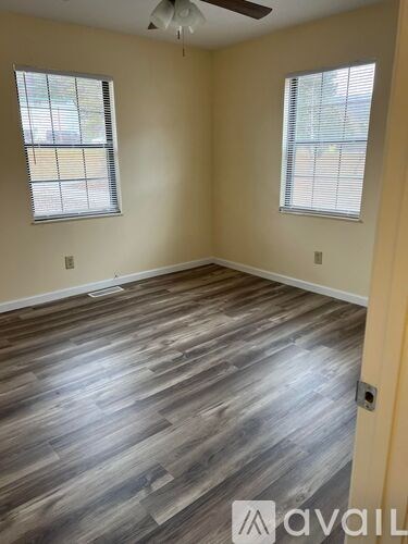 A room with wooden flooring and two windows.