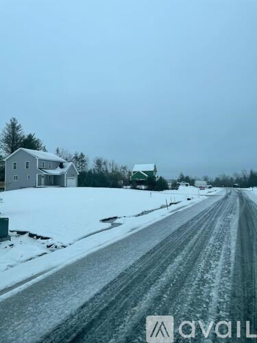 A snowy road with a house and a green building in the background.