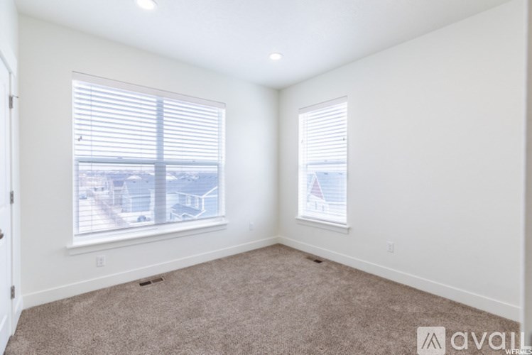 A room with carpeted floor, two windows with blinds, and a poster on the wall.