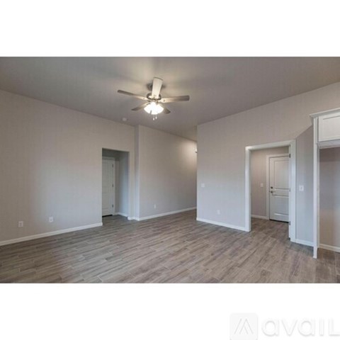 A spacious room with a ceiling fan and light fixture, and a doorway leading to another room.