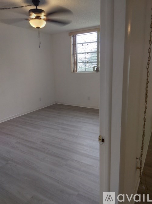 A room with a ceiling fan and light, a window with blinds, and a door with a chain.