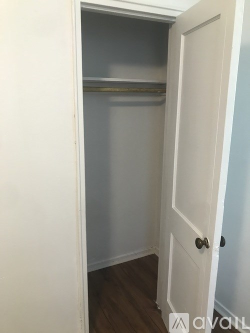 A white door is open to a small, empty room with a wooden floor.