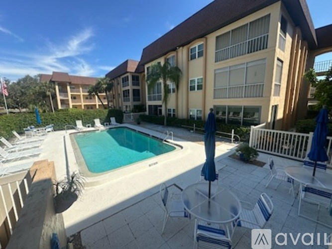 A pool area with a blue umbrella and white chairs.