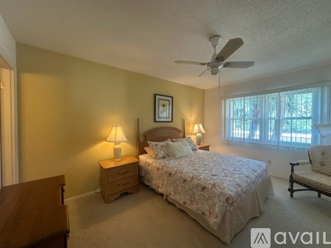 A bedroom with a bed, nightstand, chair, and a fan.