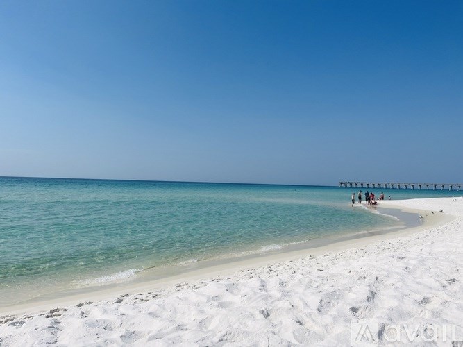 A beach with a pier in the distance and people walking on the sand.