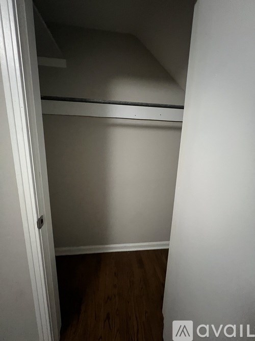 A small, empty room with a single bed and wooden flooring.