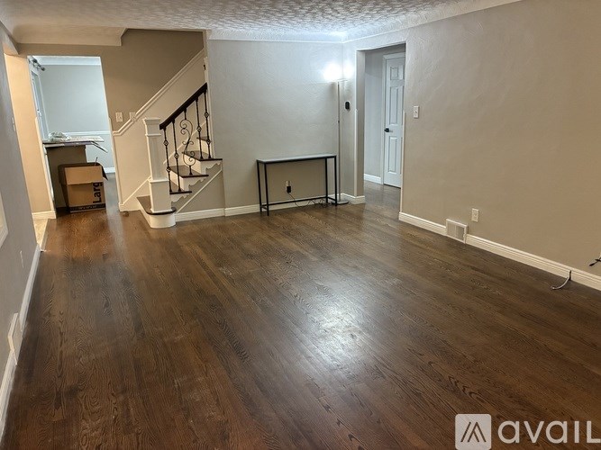 A spacious living room with wood flooring and a staircase in the background.